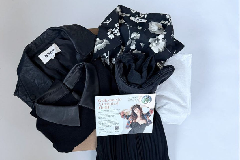 Goth all black outfit consisting of pleated skirt, black top, pants and a dress folded in a box with a postcard