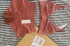 A flat lay of a pink bralette and matching briefs, mailer, and notecard on top of a stripe background