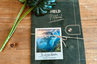 A close-up of the front of the rainforest Eco Explorer field notebook with a plastic plant, sitting on a wooden table.
