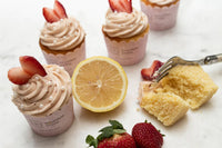 Bright lemon cupcakes topped with pink strawberry buttercream swirls and white sugar pearls in a baking kit setup