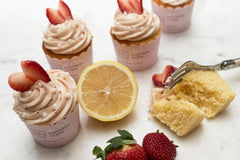 Bright lemon cupcakes topped with pink strawberry buttercream swirls and white sugar pearls in a baking kit setup