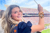 Woman at a football stadium smiling and holding up her wrist wearing the Game Day stackable friendship bracelet set with colorful beaded bra