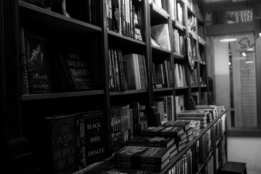 High quality image of a black and white bookshelf with hundrets of books next to each other and a glass in the background.