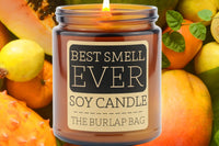 Best Smell Ever 9oz soy candle by The Burlap Bag, amber jar with a black label, set against papaya, guava, and citrus fruit