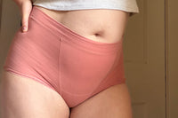 Customer posed facing forward wearing a pair of high waisted pink briefs one of the subscriptions that they received