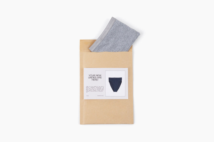 Pair of underwear (gray thong folded) peaking out of mailer along with a notecard from the subscription