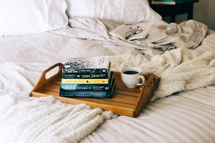 bright photo of a wooden board with four books on top of each other and with a coffee on the right side