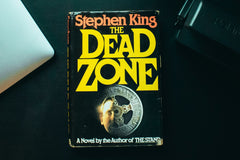 Close up image of a simple one book called the dead zone from an author named Stephen King with a macbook next to it.