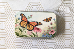 Outside label of one of the catnip tin variants. Featuring two monarch butterflies flying in a field of flowers.