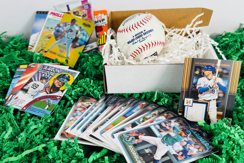 Baseball cards from a subscription box, arranged on a green grass base, with a box and baseball with the cards