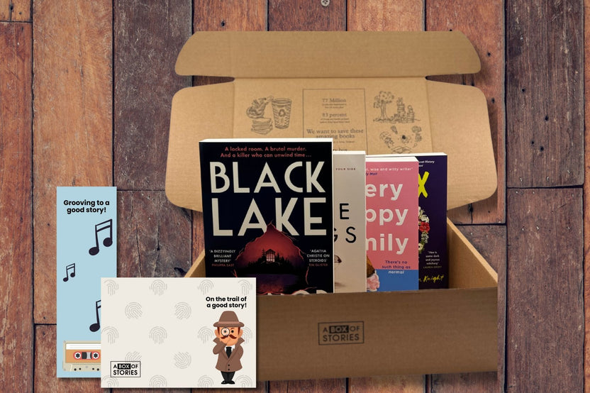 Brown box filled with a diverse collection of books in multiple genres, including crime thrillers, romance, and fantasy