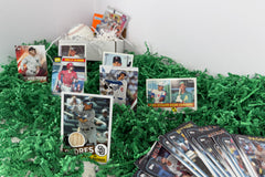 Baseball cards from a subscription box, arranged on a green grass base, with a box and baseball with the cards
