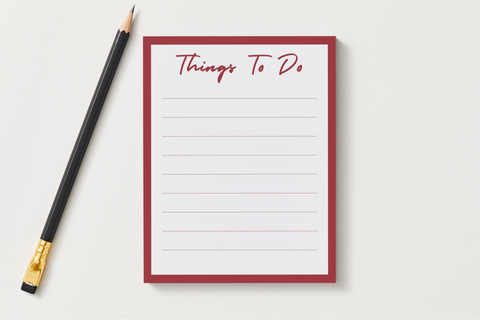 Things To Do notepad with a deep red border and lined pages, shown next to a black pencil on a soft gray desk