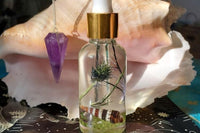 This image depicts an up close version of the magickal Piscean Anointing Oil and the Amethyst Pendulum against a conch shell. 