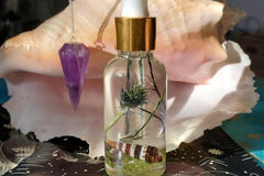 This image depicts an up close version of the magickal Piscean Anointing Oil and the Amethyst Pendulum against a conch shell. 
