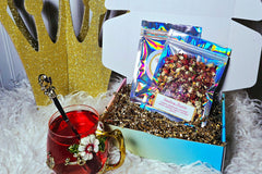 A shot of The Little Tea Box with a cup of my Strawberry Moonrise sitting  in front of it. There's a decorative crown behind the box.