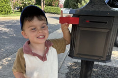 A smiling boy raises the red flag on the family mailbox, ready to send his reply to Zip, the friendly stamp who lives in the mailbox.