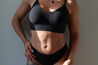 A woman posed with her hand on her hip, wearing a black seamless bralette and a matching black seamless thong