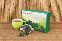 The Tea Smith tea of the month box with a tipped over tea infuser full of tea and a green tea cup full of tea.
