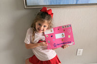 A smiling girl holds up the bright pink, sticker-covered Zip's Mailbox Club envelope that arrived in the mail with her name on it.