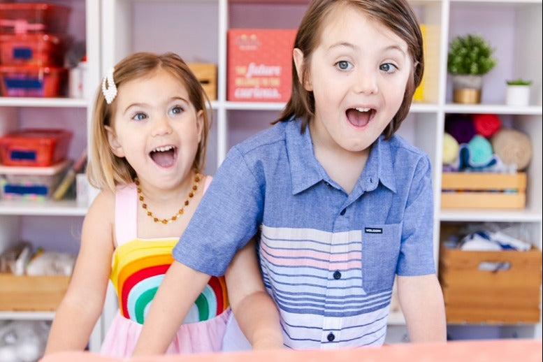A young girl and a young boy standing in front of a shelf with supplies on it looking excited about their GIGIL STEM Kit.