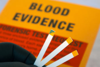 forensic tests for blood using test strips. One strip is blue for positive. An evidence envelope is in the background