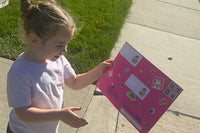 A young child on the sidewalk studies her pink Zip's Mailbox Club envelope, covered in stickers and real postage stamps, before opening it.