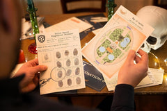 A person holding 2 papers with text and photos that are part of a mystery detective escape game with a skeleton next to it.