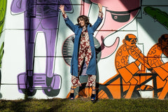 Woman jumping up and down wearing a vintage trench coat, velvet platform heels and a printed jumpsuit