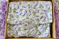 A purple box covered with lavender tissue paper and thank you sticker, with a crinkled paper around.