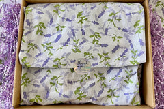 A purple box covered with lavender tissue paper and thank you sticker, with a crinkled paper around.