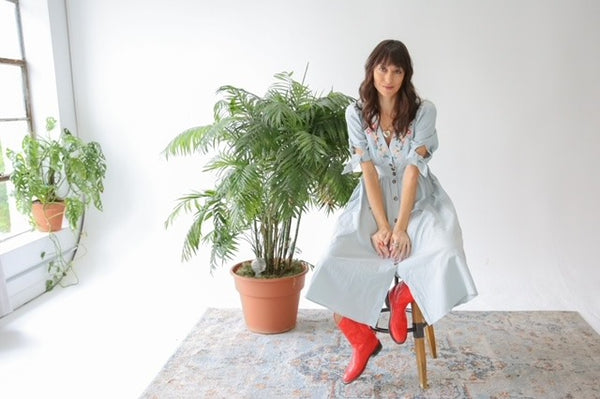 a beautiful cottagecore embroidered vintage dress and red cowboy boots to match on a model in front of a window