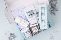 A person holds a teal Bath Bevy monthly subscription box tied with a red ribbon, ideal for self care gifts