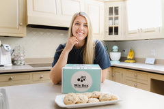 Owner Katelyn with blue Mix Boxes and cookies on a tray. Katelyn standing in her kitchen