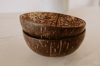 two coconut shell bowls stacked on top of one another on a white countertop, as a sustainable dining option