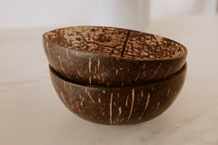 two coconut shell bowls stacked on top of one another on a white countertop, as a sustainable dining option