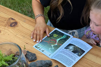 A photo of a mother and daughter reading the paperwork included in the box. There is a finished terrarium on the table aswell.