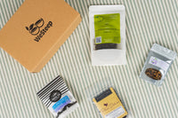 WeSteep Monthly Tea Box on a picnic blanket surrounded by loose leaf tea pouches as featured in the box.