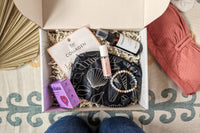 The open Palm People subscription box shows the following products: shower steamer, bracelet, small bag, tanner, perfume, and face mask.