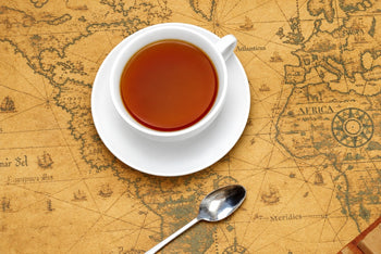 Image featuring a white tea cup with tea in it and saucer with a silver spoon on an old brown antique map. 