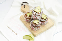 Mini golden apple cakes studded with apple bits, dusted with sugar, alongside muffin pan and baking tools