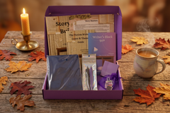 Open Journey Box on a rustic wood table with a candle, coffee, and autumn leaves, revealing the workbooks, journal, pens, and notes inside.