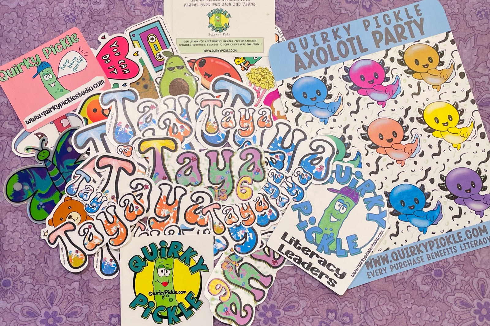 Personalized die cut stickers for subscriber Taya are shown, as well as a sheet of colorful axolotl stickers and other die-cuts from a pack.