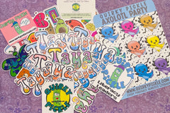 Personalized die cut stickers for subscriber Taya are shown, as well as a sheet of colorful axolotl stickers and other die-cuts from a pack.