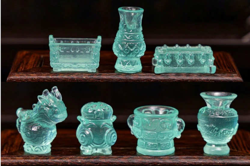 This is a photograph of a tiny miniature collection of pastel green glassware organized on a curio cabinet shelf.