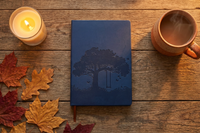 Navy 'Tree of Life' hardcover journal with an embossed tree design, flat-lay on a wood table with a candle, coffee, and autumn leaves.