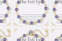Detail close-up of a single 14K gold plated evil eye bracelet on 'The Evil Eye' gift card, showing blue evil eye charms on a gold-tone chain