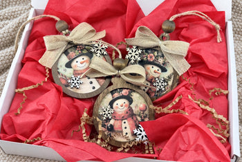 One season's shipment: three framed snowman art ornaments with jute bows and wooden beads on red tissue in an open white mailer
