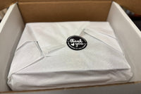 We carefully package each month's box. Image shows a set of books wrapped in white tissue paper with a thank-you sticker.