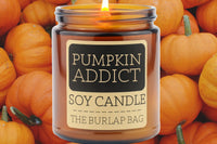 Pumpkin Addict 9oz soy candle by The Burlap Bag, spiced pumpkin scented amber jar set against a pile of small orange pumpkins